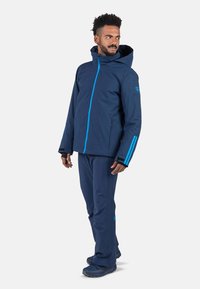 Marineblauer wasserdichter Anorak und Hose mit blauen Akzenten, Kapuze und Reißverschlusstaschen. Weicher Stoff mit figurbetontem Design für den Einsatz im Freien.