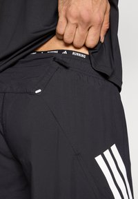 Čierne športové šortky s textúrovaným povrchom, s bielym logom adidas na boku a elastickým pásom s nápisom "RUNNING".