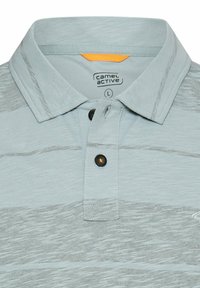 Lysegrå polo-shirt med diskrete horisontale striber, to sorte knapper og Camel Active-mærke indeni kraven.