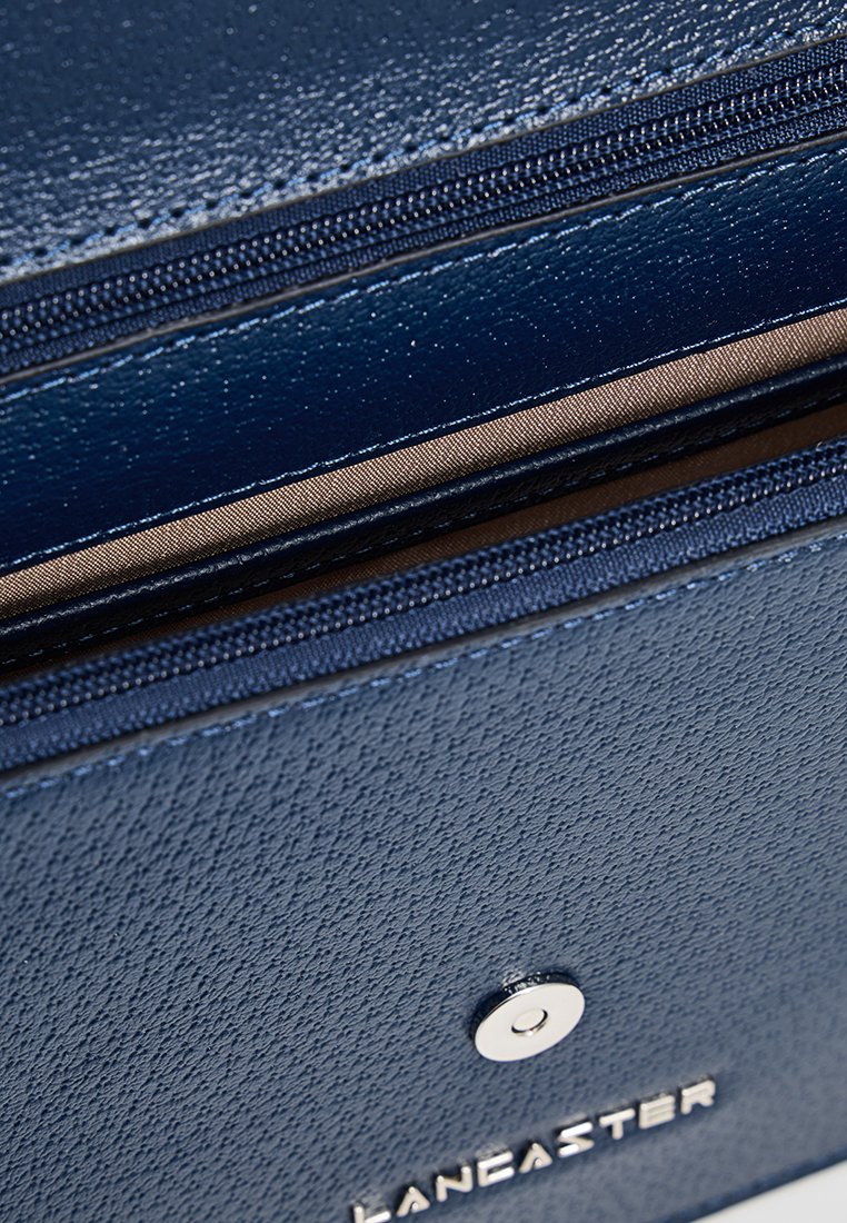 Dunkelblaues Portemonnaie aus strukturiertem Leder. Verfügt über einen silbernen Druckknopf und Reißverschlussfächer. Das Innenfutter ist hellbraun.