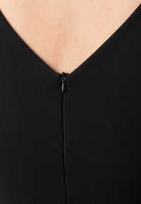 Prenda negra con un escote en V profundo, que cuenta con una pequeña cremallera en la parte posterior. Textura suave con una silueta ajustada.