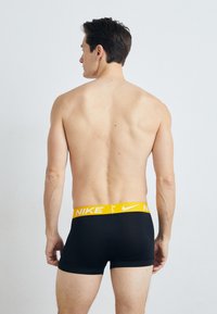 Svart boxertruser med en gul Nike-linning, med en jevn stoffstruktur. Vist fra baksiden, som viser minimale designdetaljer.