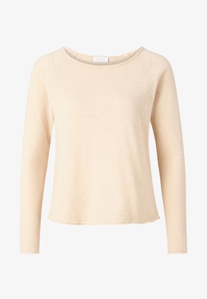 Haut beige à manches longues en tissu doux, avec un col rond et un ourlet incurvé, présentant un matériau légèrement texturé et des manches raglan.