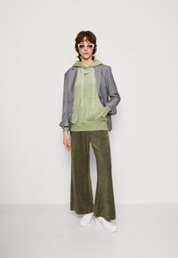 Zaļš velūra kapuces krekls ar baltām auklām, savienots ar olīvu krāsas platajām biksēm un pelēku žaketi. Balti tenisi ar rozā akcentiem papildina izskatu.