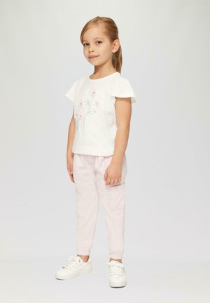Biała koszulka z krótkimi, rozszerzającymi się rękawami oraz różowymi kwiatowymi haftami, w komplecie z jasnoróżowymi spodniami; całość dopełniają białe sneakersy.