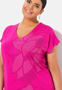 Fuchsiový top s výstřihem do V a krátkými rukávy, zdobený kovovými hroty květinových vzorů na přední straně, hladká tkanina a uvolněný střih.