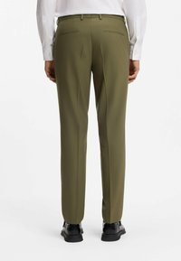 Pantalones a medida de color verde oliva con diseño de pierna recta, con una textura suave y dos bolsillos traseros. Combinados con zapatos negros.