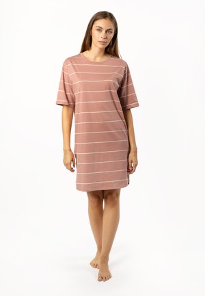 Young woman standing barefoot wearing a loose dusty pink T-shirt dress with thin white horizontal stripes on a white background.