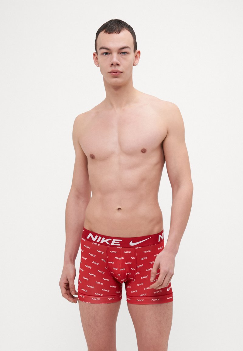 Czerwone bokserki Nike z białą elastyczną taśmą z logo i powtarzającym się wzorem. Materiał wydaje się gładki i dobrze dopasowany.