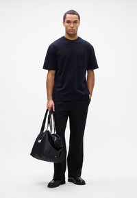 Μαύρο βαμβακερό t-shirt με τσέπη, συνδυασμένο με μαύρο παντελόνι και μαύρη τσάντα. Η τσάντα διαθέτει λευκό λογότυπο και ριγέ λαβές. Λείος υφή.