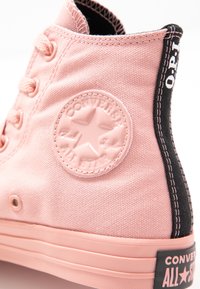 Różowe płócienne trampki typu wysokiego z uniesionym logo gwiazdki, czarną wykończeniem kostki i kontrastowym przeszyciem. Gumowa podeszwa z detalami marki.