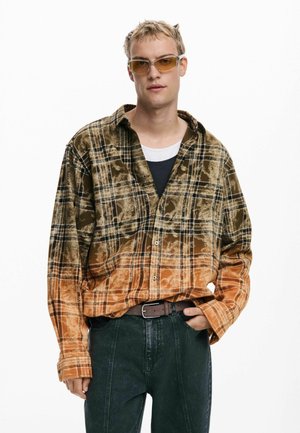 Brown and orange plaid flannel shirt with a slightly faded texture, paired with dark denim pants. Model wears light-colored sunglasses.