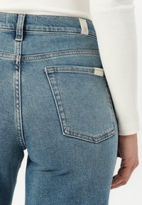 Lys blå denimjeans med høy midje og baklommer. Klassisk søm og en liten etikett på livet.