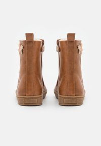 Botas de tobillo de cuero marrón con cremalleras laterales, una superficie texturizada, una suela de goma de contraste más clara y acentos decorativos en forma de mariposa.