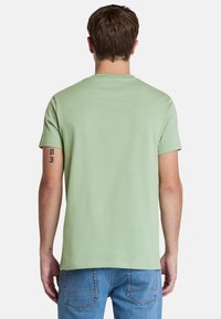 Camiseta de manga corta en verde menta de algodón suave con cuello redondo, detalle en la costura trasera y corte relajado. Se combina con unos vaqueros de denim azul.