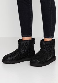 Botas de tobillo negras hechas de ante texturizado, con un diseño estampado que incluye letras en relieve y una suela de goma plana.