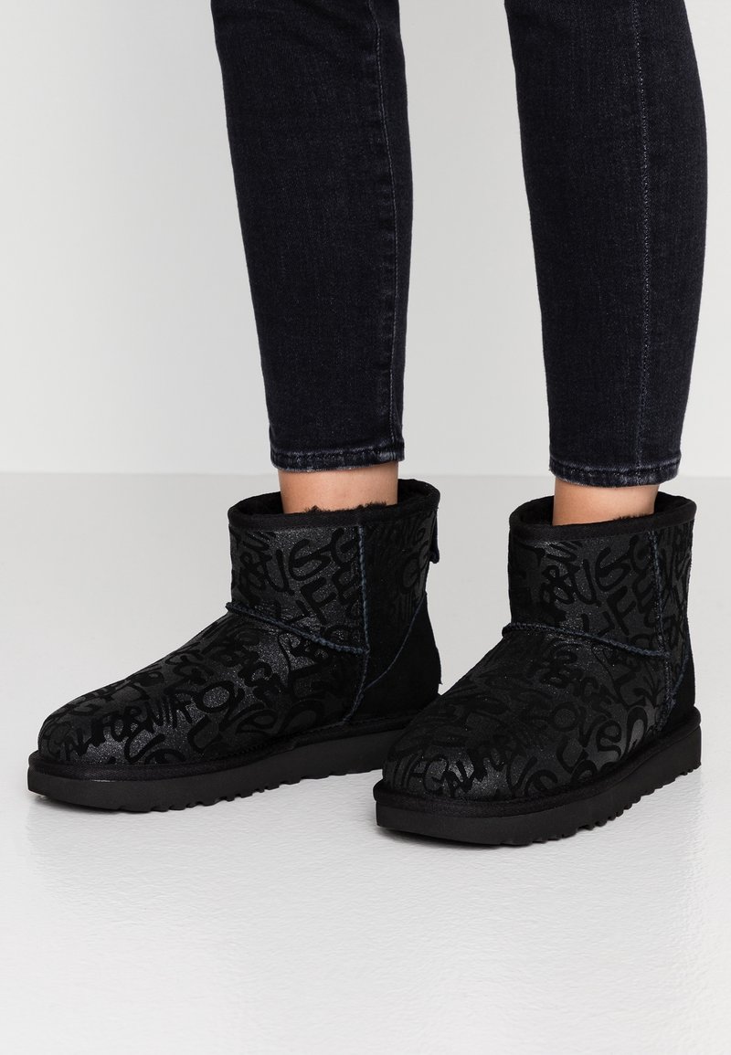 Botas de tobillo negras hechas de ante texturizado, con un diseño estampado que incluye letras en relieve y una suela de goma plana.