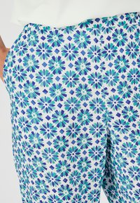 Bloemmotief broek met een witte achtergrond, voorzien van blauwe en groene bloemen en diamanten vormen, gladde textuur, elastische tailleband.