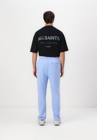 Black oversized t-shirt with white text and graphics on the back, paired with light blue sweatpants featuring a side pocket.