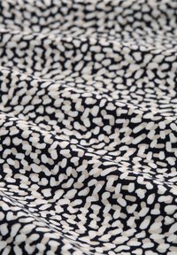 Schwarzer Stoff mit einem weißen und beigefarbenen abstrakten Muster, das eine strukturierte Optik und eine glatte Oberfläche aufweist. Sanfte Variationen in der Musterdichte.