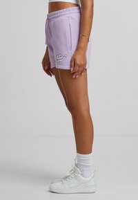 Lila bomullsshorts med elastisk midja, sidofickor och vitt broderat logotyp. Matchas med vita sneakers och ankelsockor.