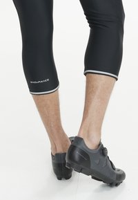 Schwarze Radsportshorts mit silbernen Akzenten, mit einem Logo an der Seite. Schwarze Radsportschuhe mit Details aus Mesh und Gummisohle.