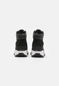Svarte høyde sneakers med overdel i semsket skinn og tekstil, polstret krage, hvit såle, teksturert svart yttersåle og bakre logo detalj.
