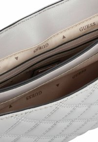 Bolso acolchado de color gris claro con un exterior de cuero liso. El interior cuenta con un forro beige con un patrón sutil y detalles del logo.