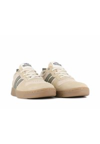 Beige mokasinit kengät, joissa on kaksi vihreää raitaa, pyöreä kärki, pehmustettu nilkkareunus ja valkoiset nauhat. Kumipohja ja logo kielellä.