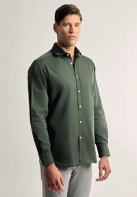 Camisa verde de manga larga en una suave mezcla de algodón, que presenta un cierre de botones en la parte delantera, cuello clásico y un sutil logo en el pecho.