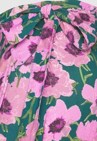 Tela floral con grandes estampados de peonías rosas y púrpuras oscuras sobre un fondo verde. Cuenta con un detalle de lazo atado en la parte superior.