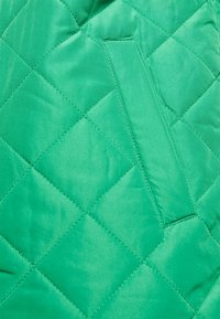 Tecido verde acolchoado com um acabamento suave. Apresenta um pequeno bolso embutido e um padrão de diamante criado por costura.