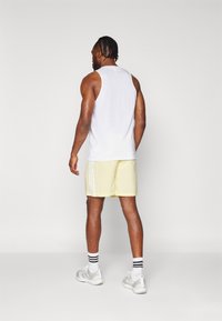 Λευκή αμάνικη μπλούζα και ανοιχτό κίτρινο σορτς με λευκές ρίγες. Το άτομο φοράει λευκά και γκρι αθλητικά παπούτσια με ριγωτές κάλτσες.