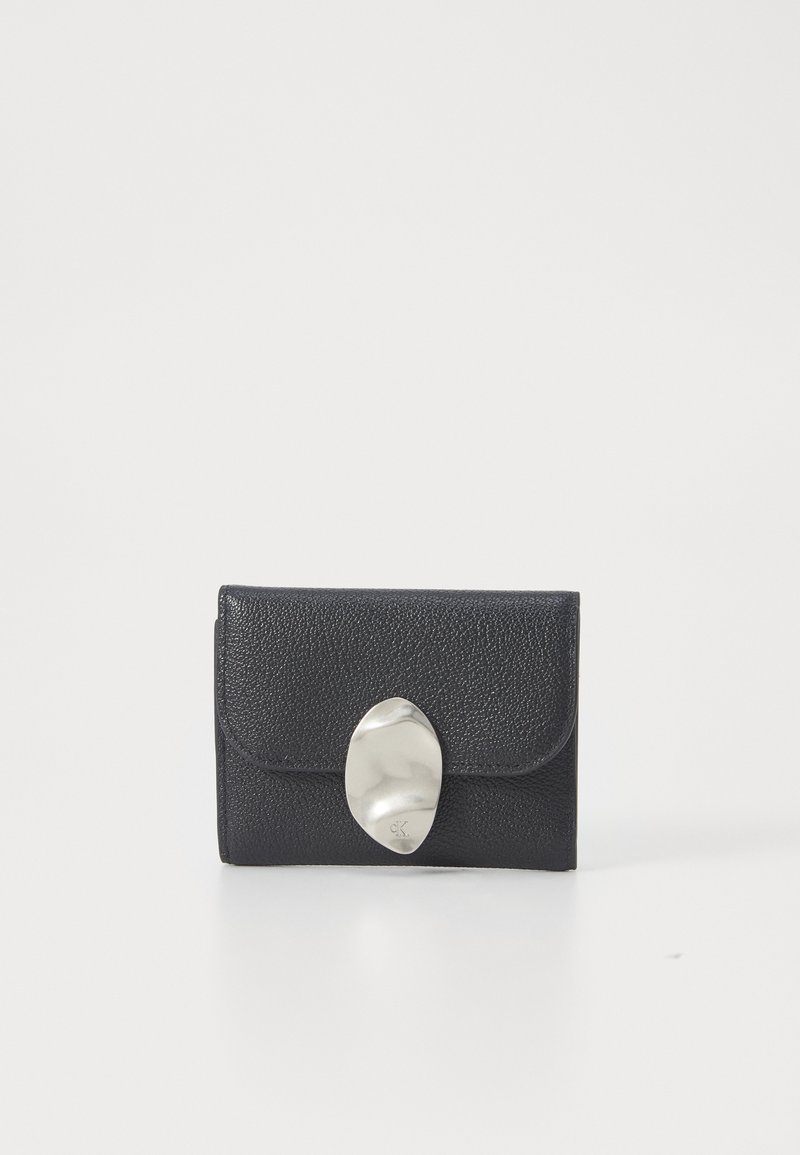 Carteira de couro preto com uma superfície texturizada. Apresenta um fecho oval metálico liso. Forma retangular compacta, design minimalista.
