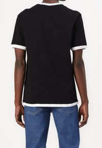 Zwarte katoenen t-shirt met witte afwerking op de kraag en mouwen, met een relaxte pasvorm. G gedragen met blauwe spijkerbroek.