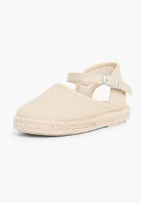 Espadrille en toile beige avec un bout arrondi, une sangle à la cheville et une semelle en jute tressé, présentant des détails cousus le long des bords.
