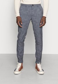 Lehké modré vzorované kalhoty, slim fit s knoflíkovým zapínáním. V kombinaci s vysokými teniskami v hnědé, bílé a modré barvě.