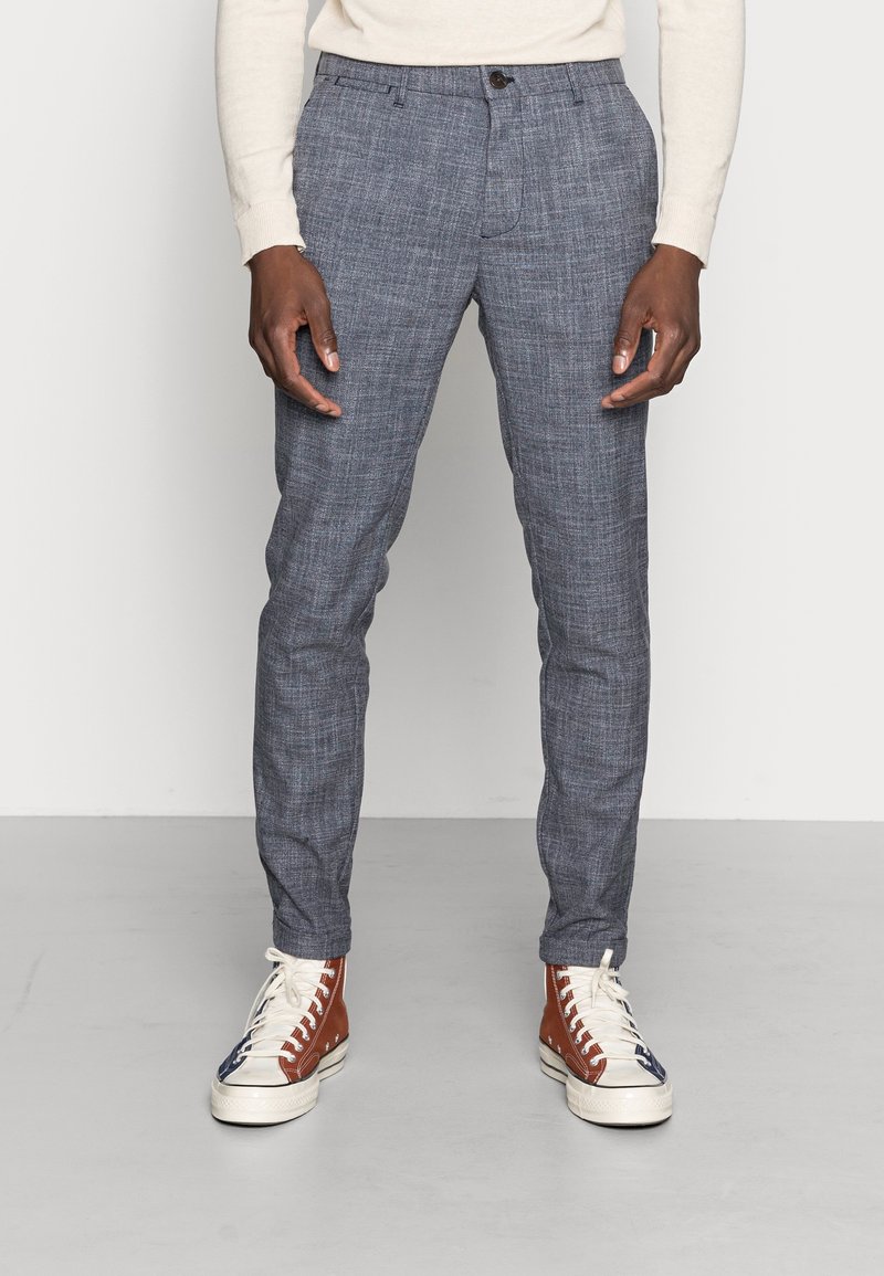 Lehké modré vzorované kalhoty, slim fit s knoflíkovým zapínáním. V kombinaci s vysokými teniskami v hnědé, bílé a modré barvě.