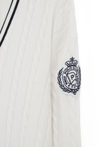 Weißer Pullover mit Strickmuster, schwarzer Einfassung und einem bestickten Polo Club-Abzeichen mit einer Krone auf dem oberen Ärmel.