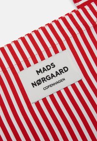 Czerwono-biała tkanina w paski, z prostokątną etykietą z napisem "MADS NØRGAARD COPENHAGEN" w wyraźnym czarnym tekście.
