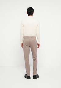 Lichtbeige langemouw shirt gecombineerd met lichtbruine broek en zwarte schoenen. De outfit heeft een eenvoudig ontwerp en een getailleerde pasvorm.