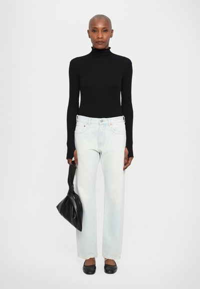 Suéter negro de cuello alto, jeans de corte ancho en azul claro, bailarinas negras y un bolso negro. La ropa presenta texturas suaves y un diseño casual.