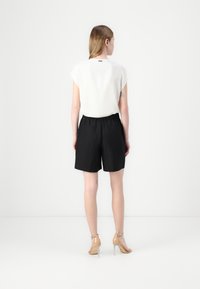 Hvit kortermet topp med rund hals, kombinert med svarte shorts med elastisk midje, supplert med beige høyhælte sandaler.