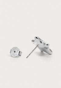 Silver stainless steel earrings featuring a smooth, organic shape with a post back. One earring has a round, branded backing.