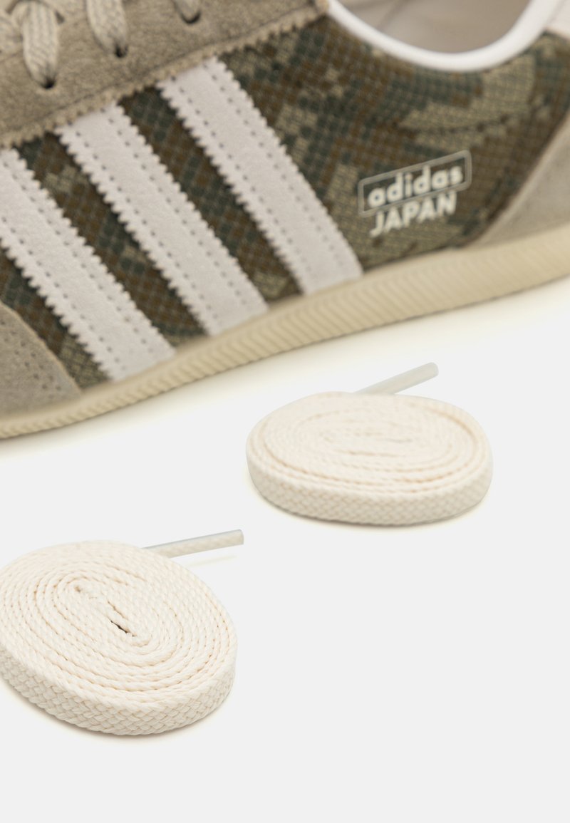 Adidas Japan sneakers hebben een bovenwerk van grijs suède met groene en bruine camouflageaccenten, drie witte strepen en worden geleverd met witte platte veters.