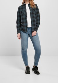 Camicia di flanella a quadri neri e turchesi sopra una t-shirt bianca, abbinata a jeans skinny blu chiaro e scarpe in vernice nera.