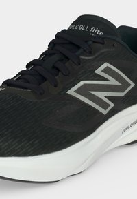 Μαύρο αθλητικό παπούτσι New Balance με γκρι λογότυπο "N", μαύρα κορδόνια και λευκή μεσόσολα με την ένδειξη "FuelCell flite" στο πλάι.