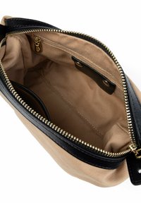 Borsa in tela con interno color sabbia e dettagli in pelle nera. Presenta una chiusura con zip dorata e una piccola tasca interna. Tessuto liscio.