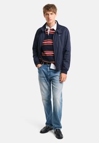 Marinefarvet bomberjakke, stribet sweater i marineblå og rød, lyseblå jeans, sorte sko. Afslappet outfit med varierende teksturer og farver.