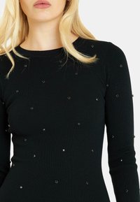 Schwarzes, geripptes Langarmoberteil mit verstreuten schwarzen Pailletten, das über einen Rundhalsausschnitt und eine taillierte Silhouette verfügt.